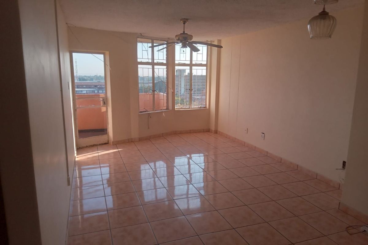An empty living area featuring tiled flooring, a ceiling fan, and direct access to an outdoor balcony through a glass-paneled door.