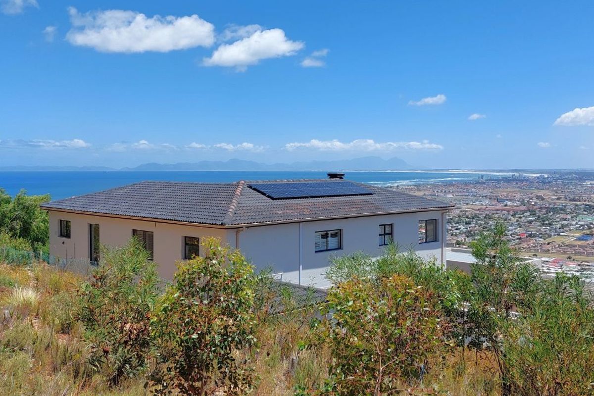 Elevated view of a residential property featuring a tiled roof with integrated solar panels, overlooking a coastal landscape and urban area.