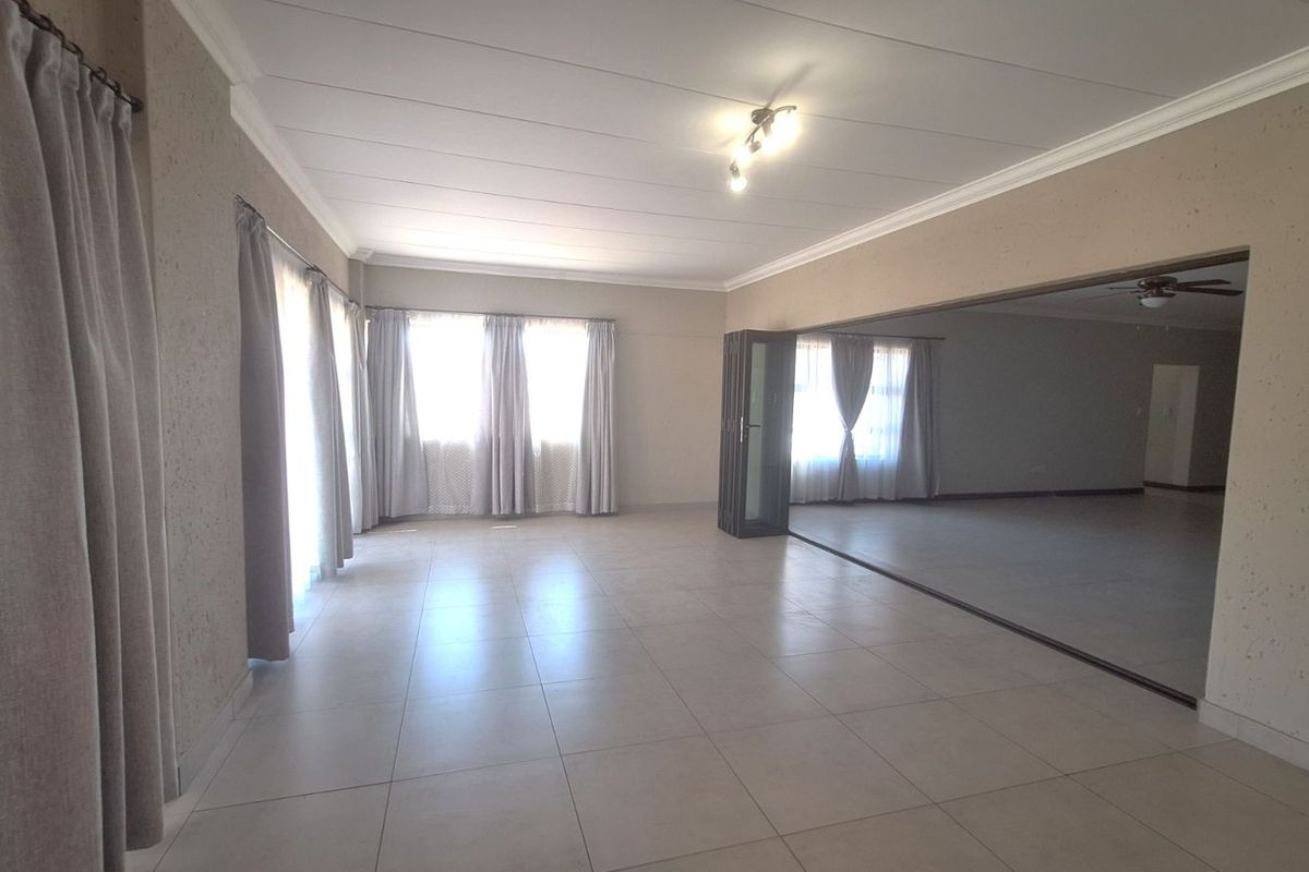 Spacious living area featuring neutral floor tiles, large windows with curtains, and a large wall-mounted mirror reflecting the adjacent space.
