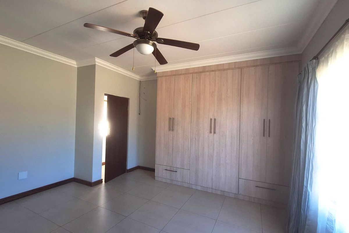 Spacious bedroom featuring light-toned built-in cupboards, tiled flooring, and a ceiling fan, offering a clean and functional living space.