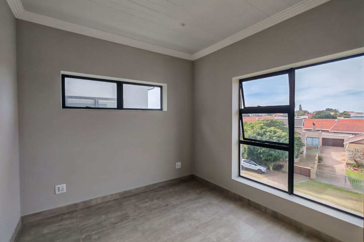A bright, empty bedroom featuring modern grey floor tiles, neutral wall paint, and large windows offering a pleasant neighborhood view.