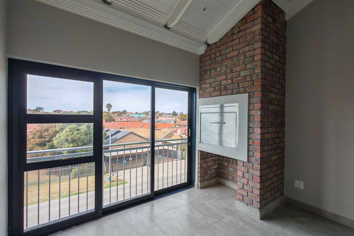 A bright living area featuring a built-in brick fireplace, tiled flooring, and large sliding doors opening onto a balcony with neighborhood views.