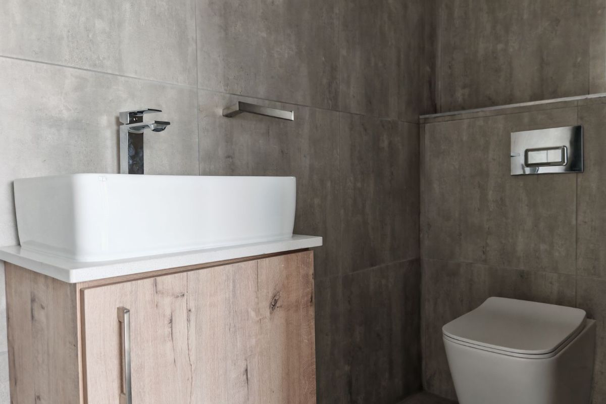 Modern bathroom featuring a contemporary vessel sink on a wood-finish vanity, wall-mounted toilet with concealed cistern, and large-format grey tiled walls.