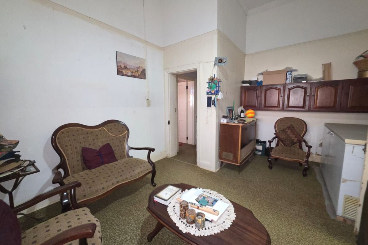 A dated living area featuring high ceilings, wall-mounted cabinetry, and original carpet flooring, requiring significant cosmetic updates and modernization.
