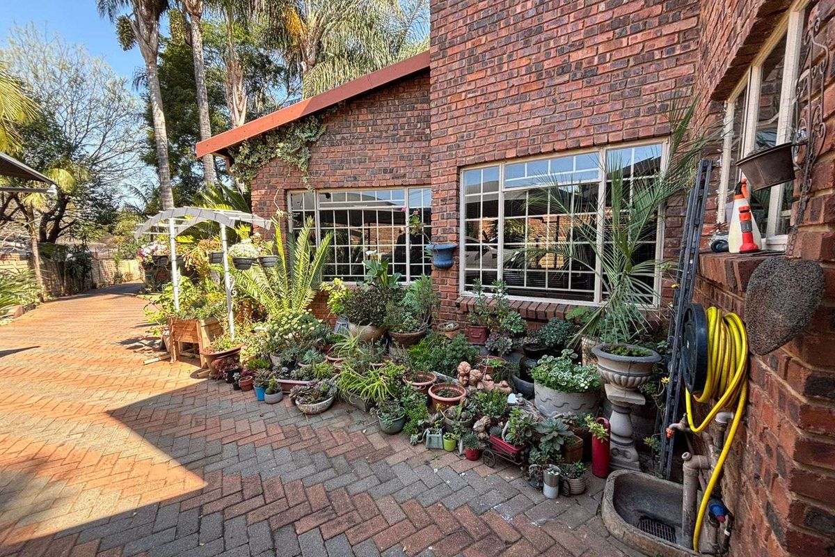 A paved side exterior area featuring exposed brick walls, large grid-style windows, and a functional outdoor water tap with hose connection.