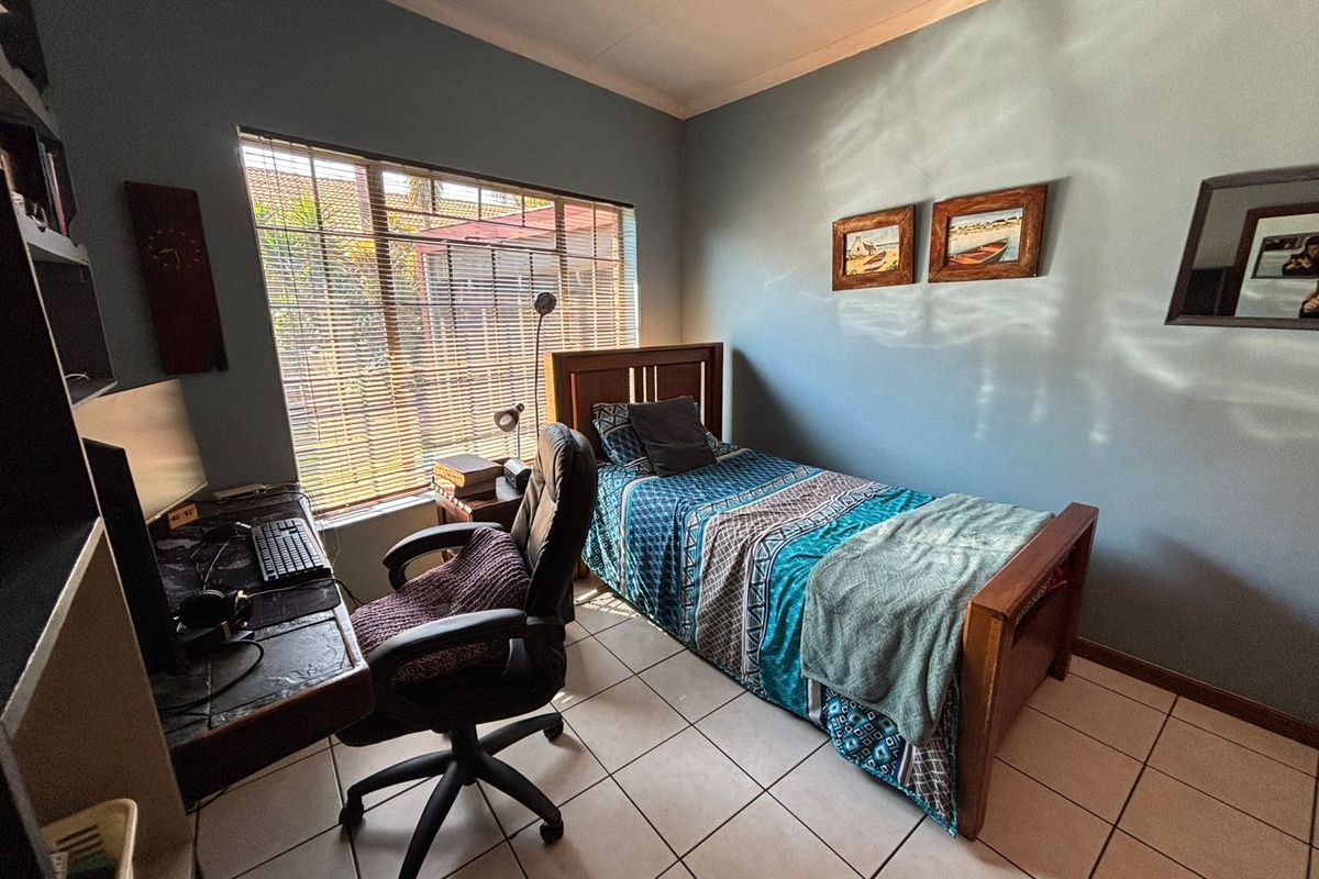 A functional bedroom featuring tiled flooring, a large window with fitted blinds, and neutral wall finishes.