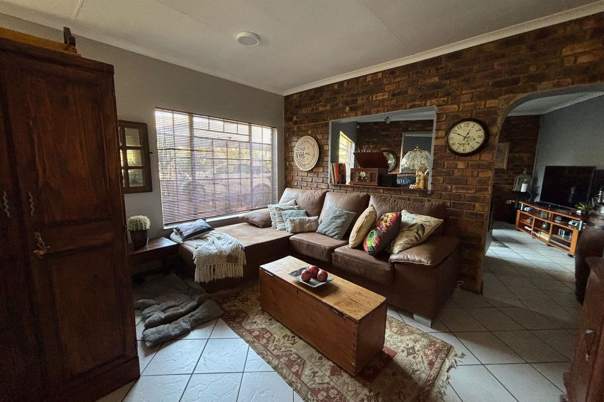 A cozy living room featuring a prominent exposed brick feature wall, tiled flooring, and a large window with fitted blinds.