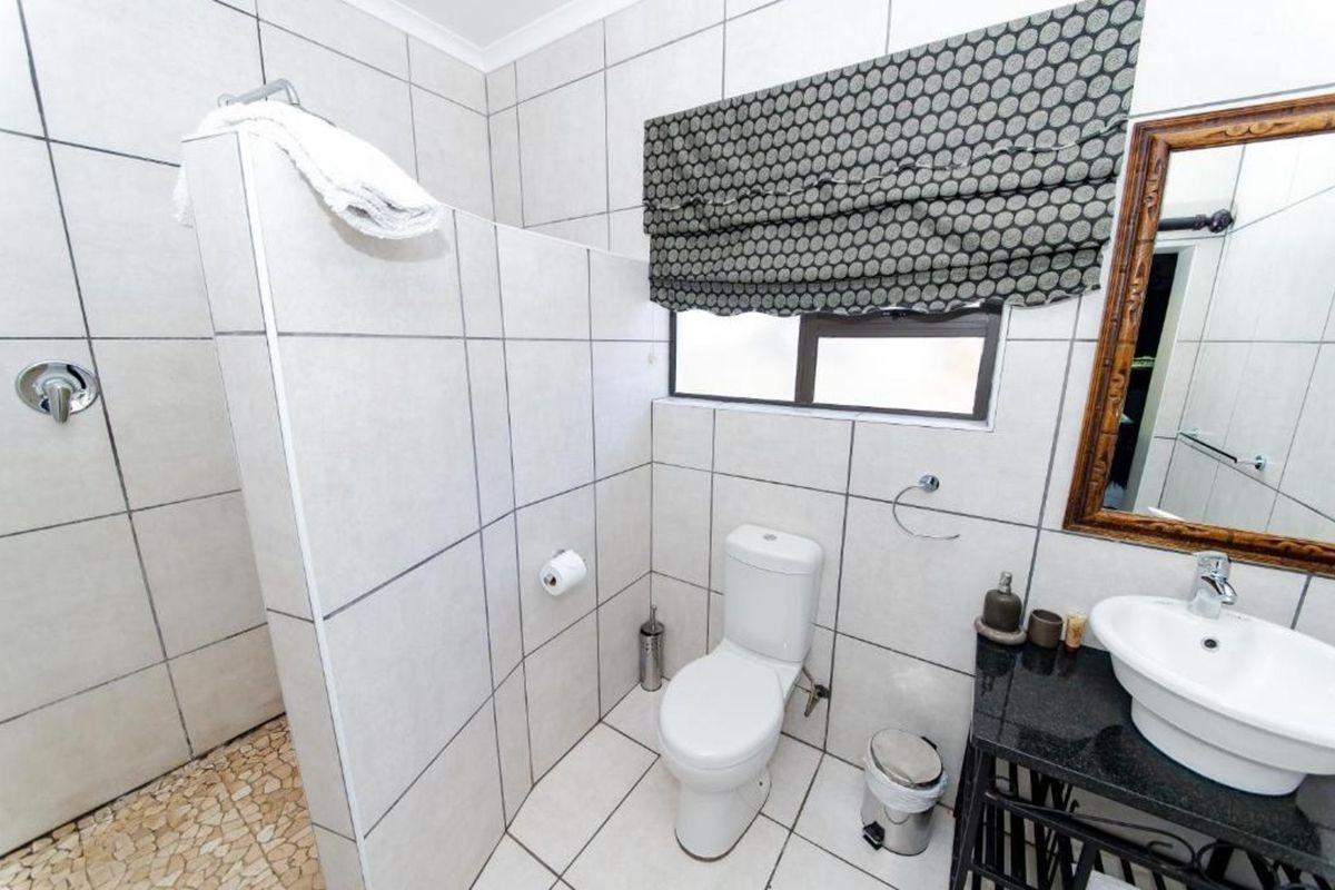 A functional bathroom featuring a walk-in shower with tiled partition, a white toilet, and a vanity basin with a dark stone countertop.