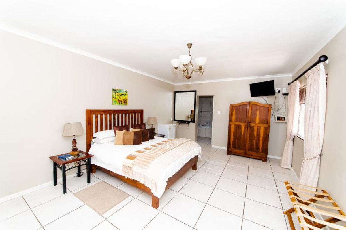 A spacious bedroom featuring tiled flooring, a ceiling-mounted light fixture, and an en-suite bathroom access point.