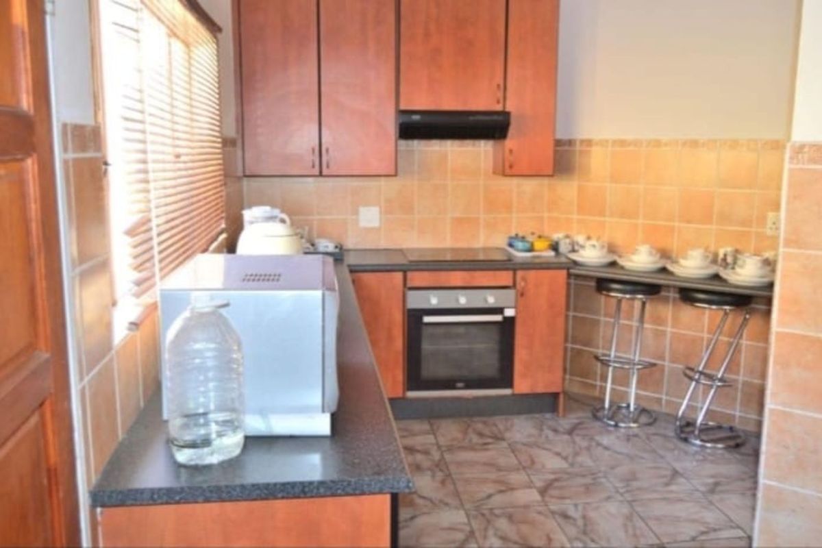 A functional kitchen featuring wood-finish cabinetry, a built-in oven, electric hob, extractor fan, and tiled splashbacks with a breakfast bar area.