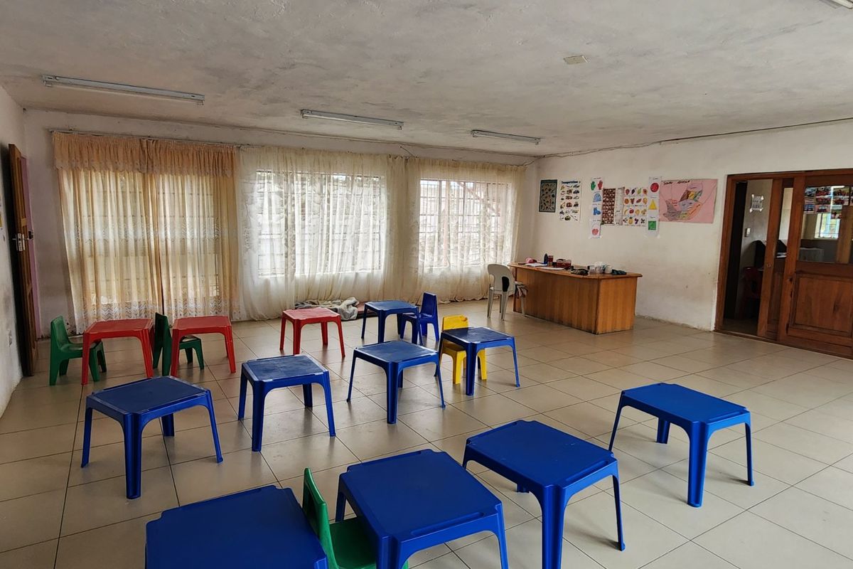 A large, open-plan room currently utilized as a classroom, featuring tiled flooring and multiple windows with curtains.