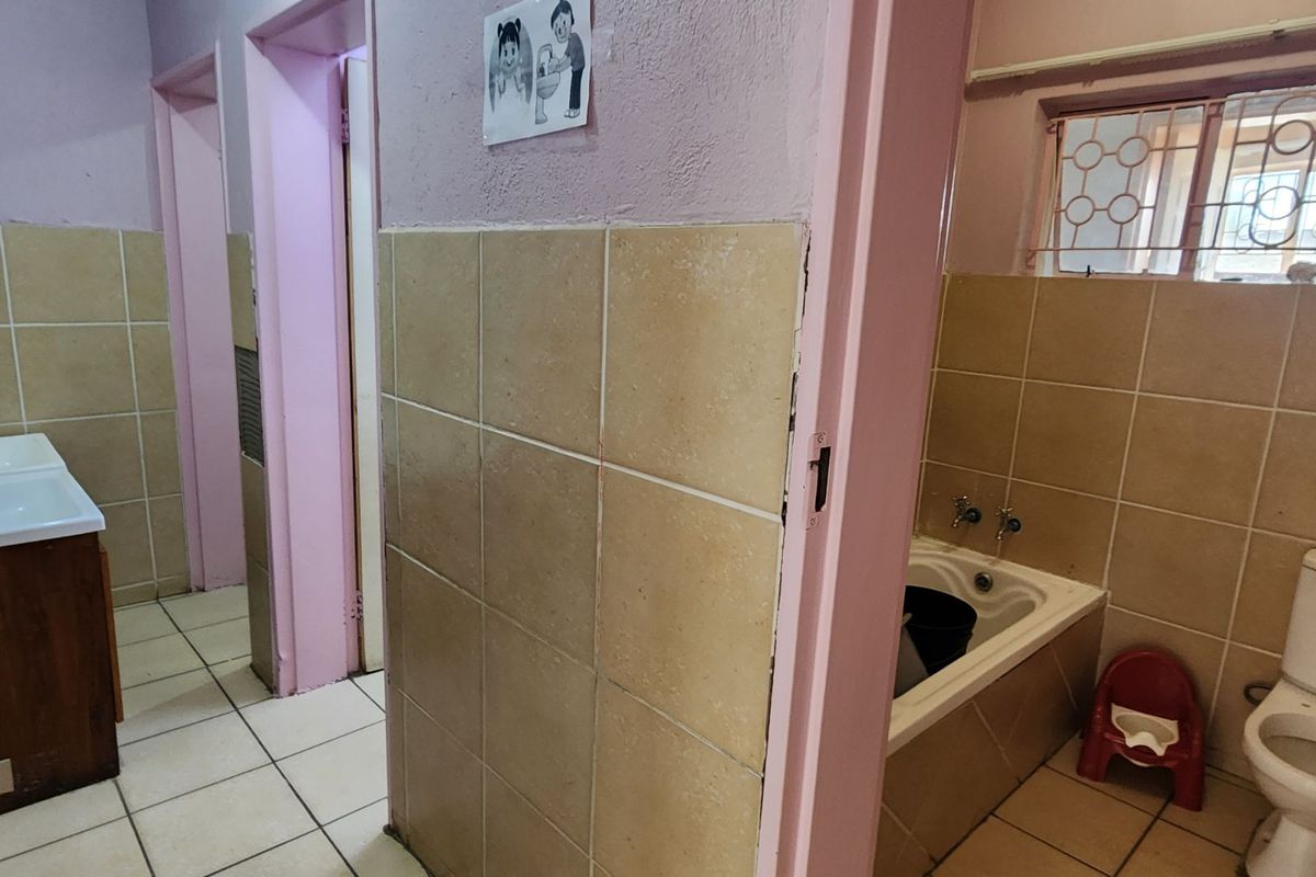 A functional bathroom featuring a built-in bathtub, toilet, and vanity, with tiled walls and flooring in a dated aesthetic.