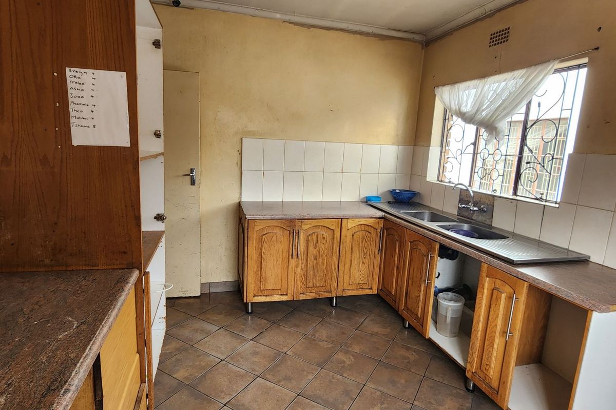 A functional kitchen featuring wooden cabinetry, tiled flooring, and a double-basin sink with a window view.