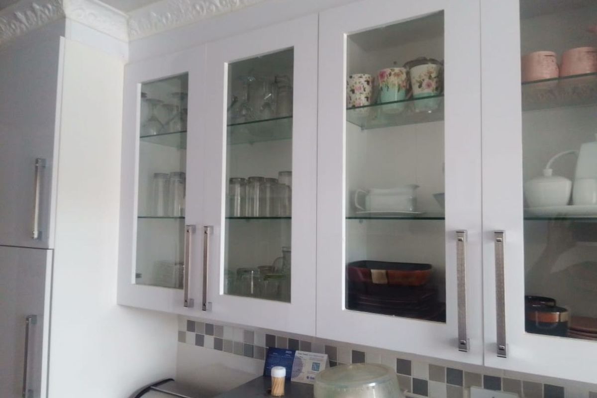 Close-up view of white kitchen cabinetry featuring glass-fronted upper cupboards, modern metal handles, and a neutral mosaic tile backsplash.