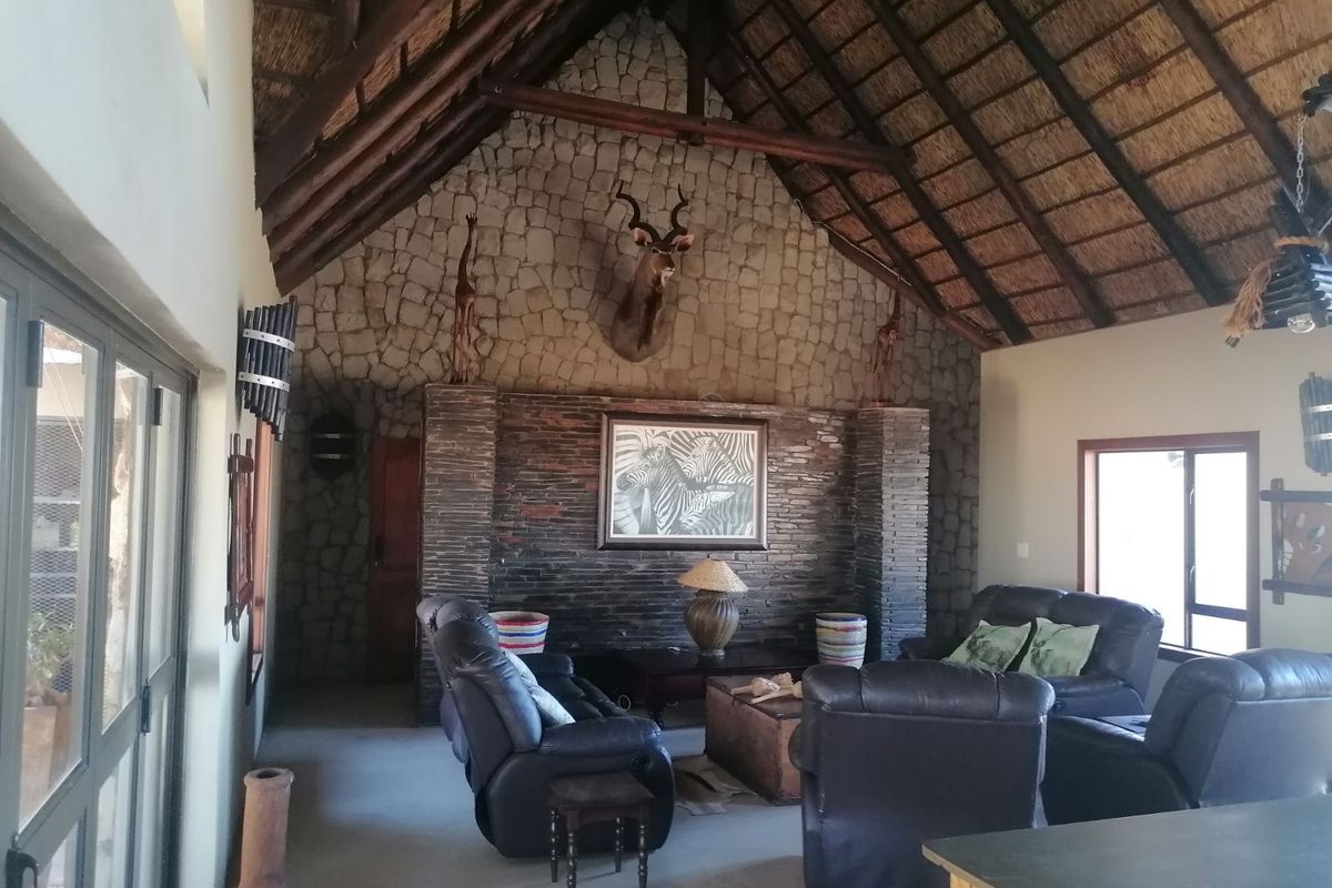 Spacious living room featuring a high vaulted thatched ceiling, exposed timber beams, and a prominent stone-clad feature wall with a built-in fireplace.