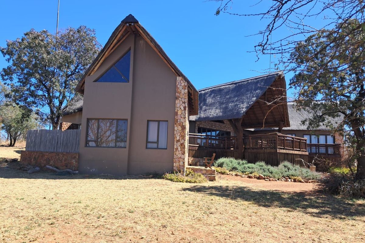 A view of the rear exterior of a house featuring a thatched roof, stone cladding accents, and a wooden deck.