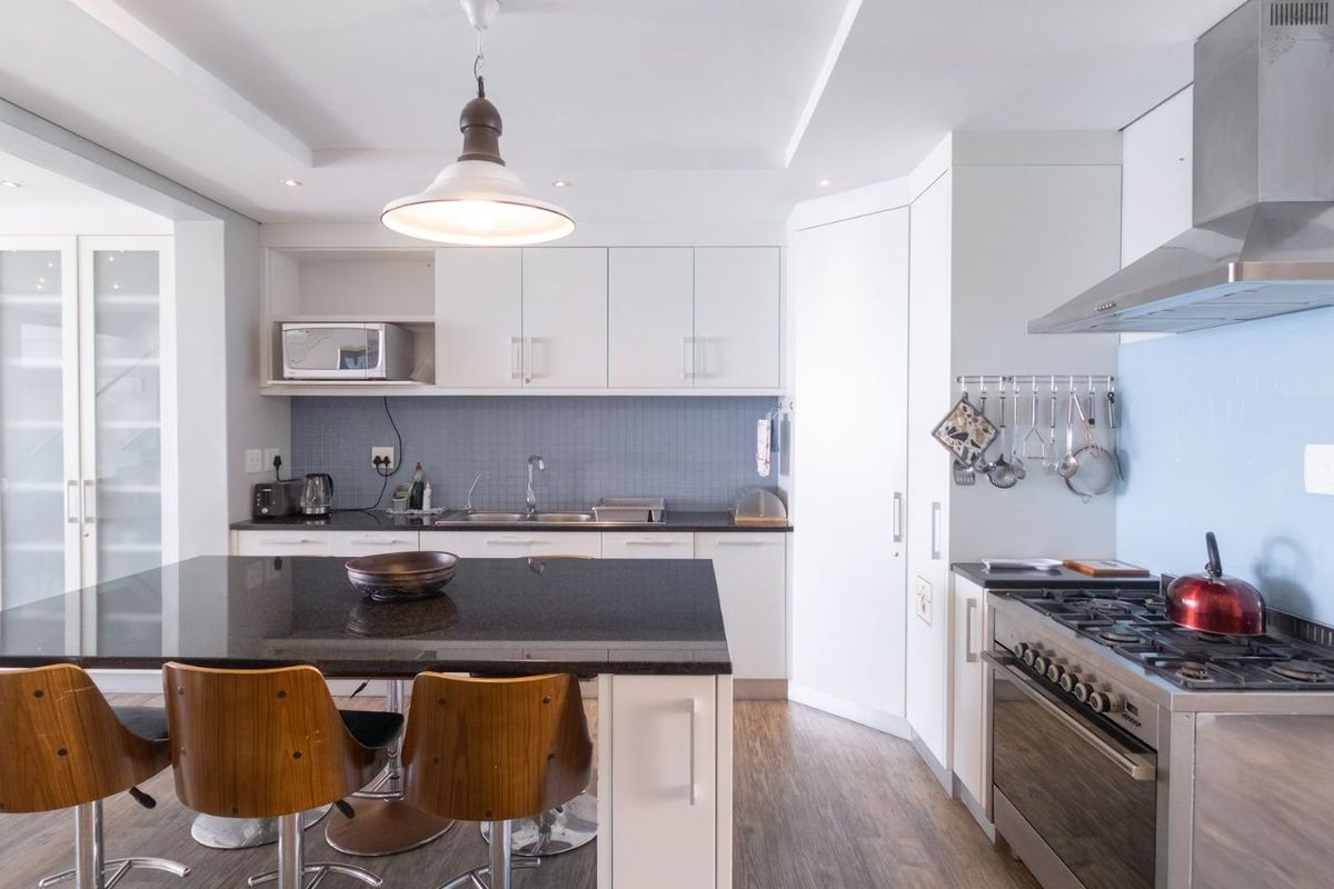 Modern kitchen featuring white cabinetry, a black granite island countertop, stainless steel gas stove, extractor fan, and tiled backsplash.