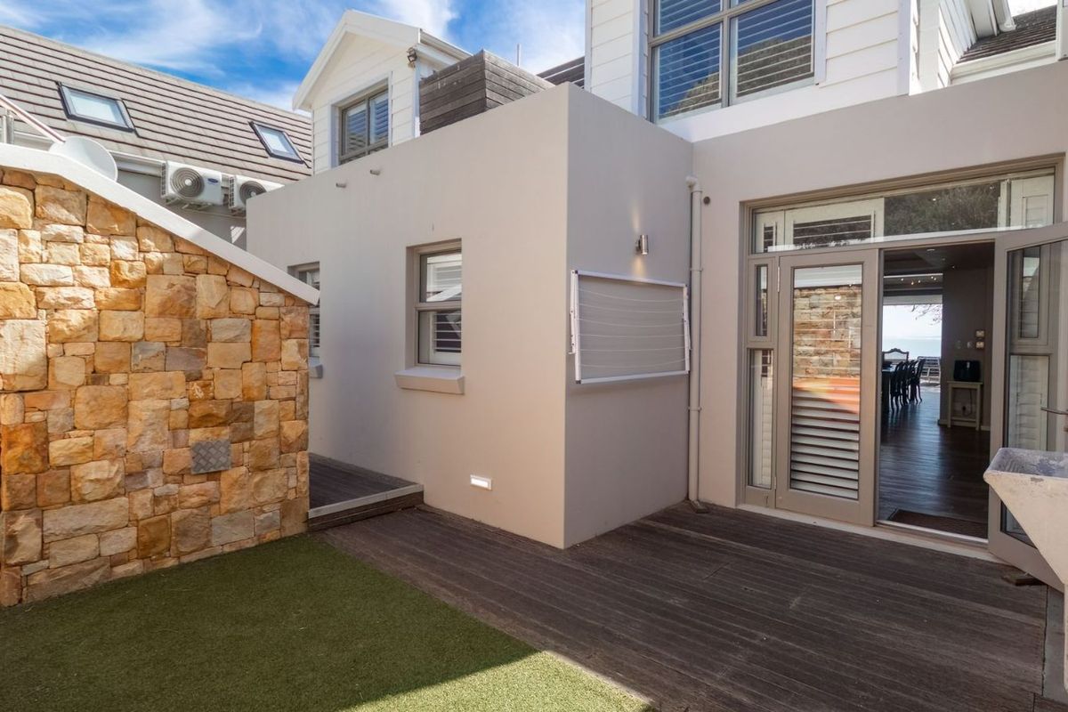 A well-maintained rear exterior area featuring a timber deck, stone cladding, artificial lawn, and a convenient outdoor utility sink.