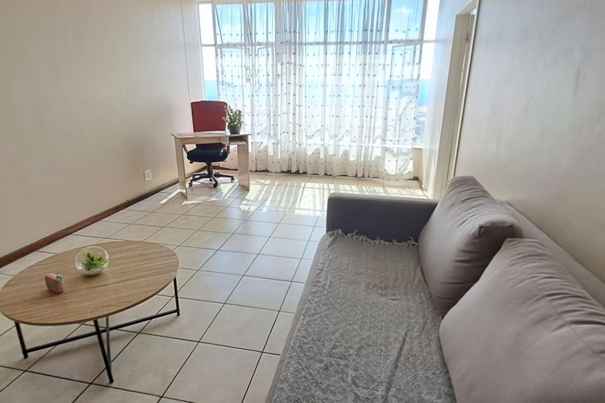 A bright living area featuring large windows with natural light, tiled flooring, and neutral wall finishes, suitable for a comfortable lounge setup.