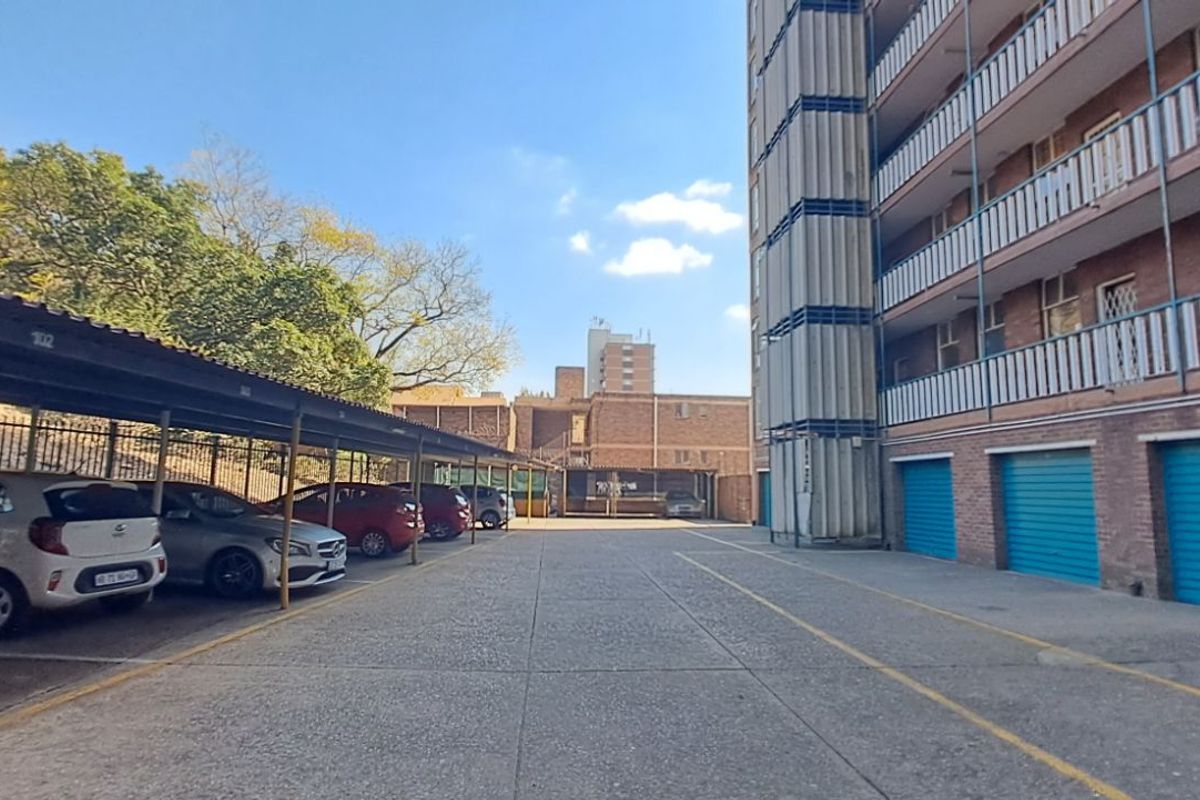 Exterior view of the apartment complex parking area featuring covered carports and ground-level garage units.