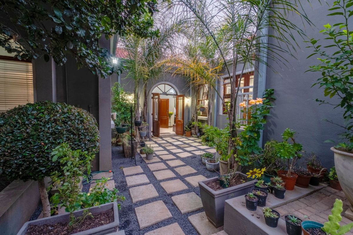 A charming, landscaped courtyard entrance featuring paved stepping stones, gravel pathways, and established greenery leading to the main arched doorway.