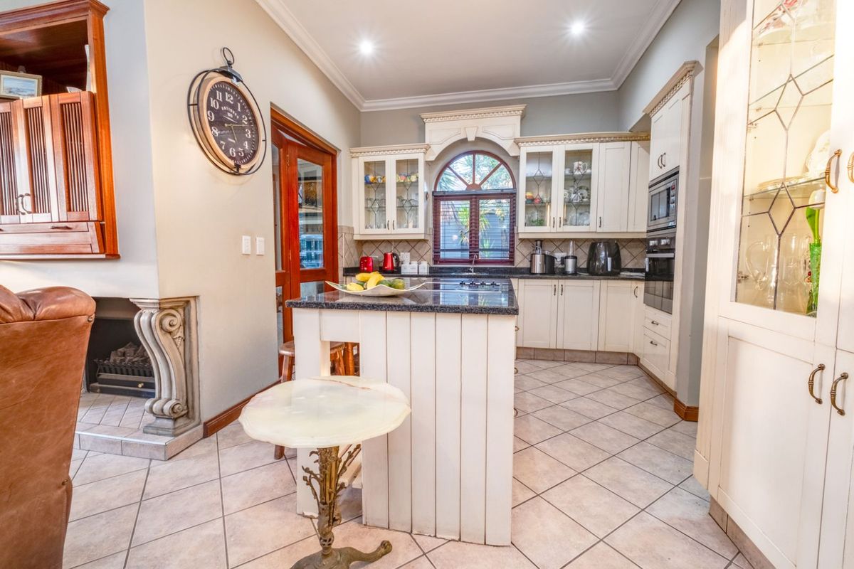 A well-appointed kitchen featuring classic cabinetry, a central island with stone countertop, built-in oven, and an adjacent fireplace with decorative mantle.