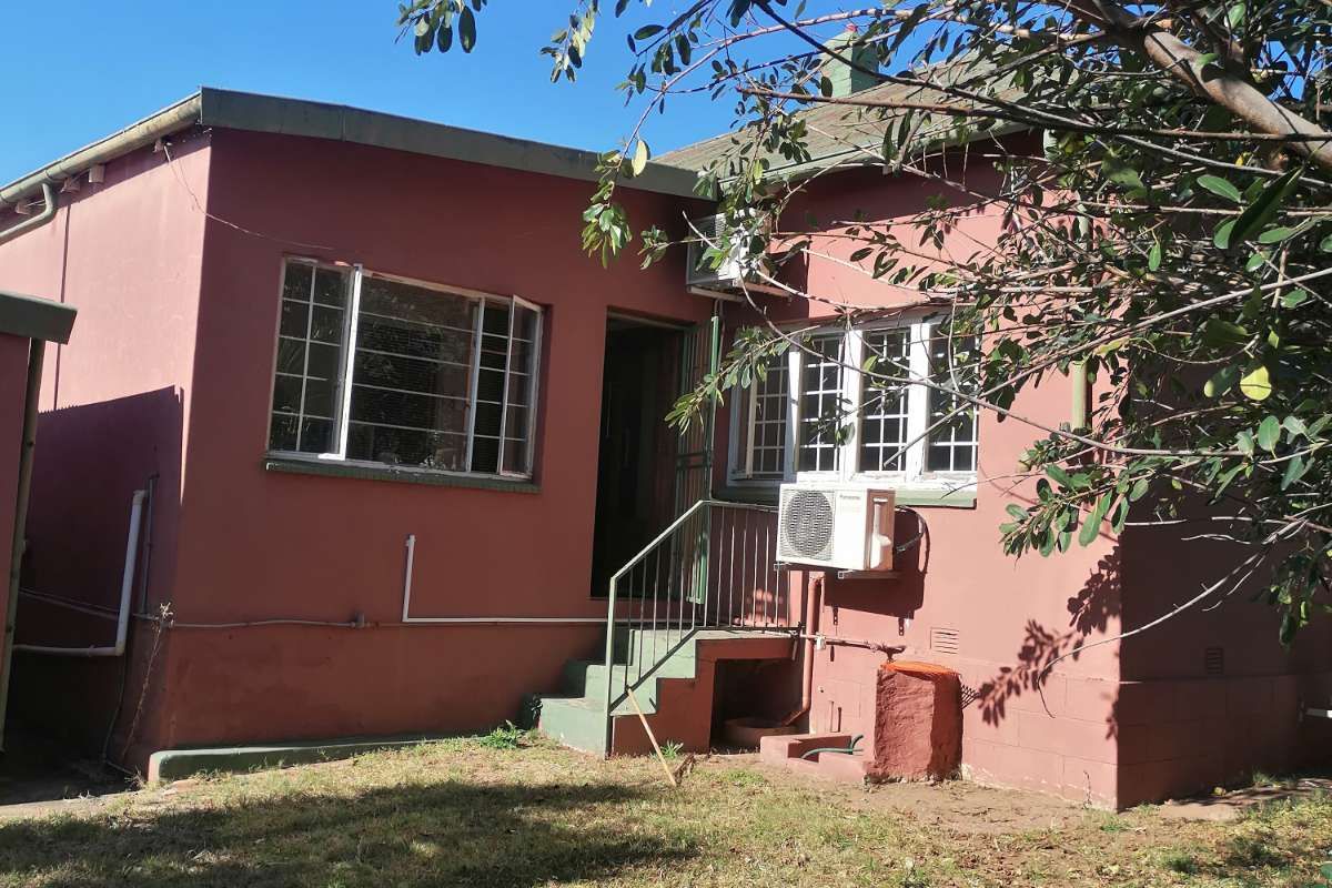 Rear view of the house featuring a small staircase, exterior air conditioning unit, and metal-framed windows set against a garden area.