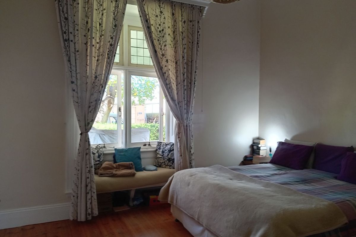 A cozy bedroom featuring polished timber flooring, a built-in window seat, and classic leaded glass window detailing.