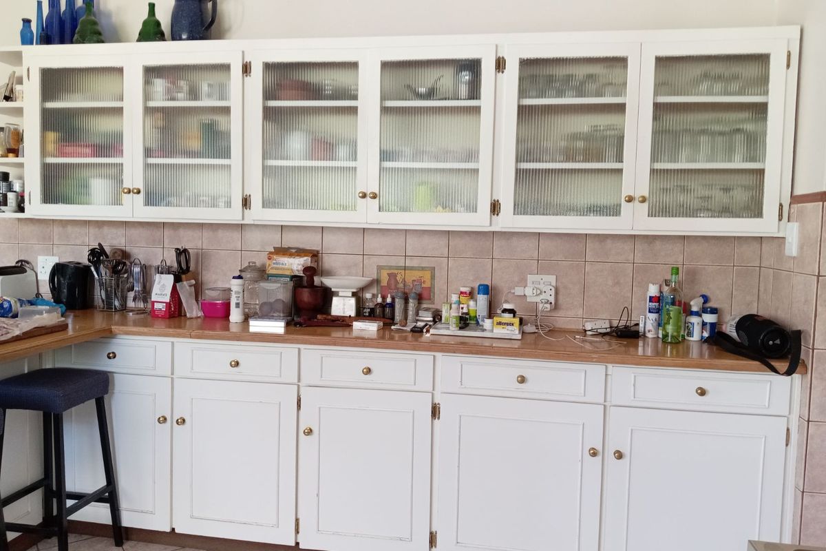 A kitchen area featuring white cabinetry with glass-fronted upper cupboards, a tiled backsplash, and a wooden countertop.