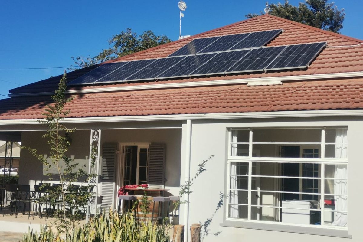 A well-maintained exterior view of the house featuring a tiled roof with installed solar panels and a covered patio area.