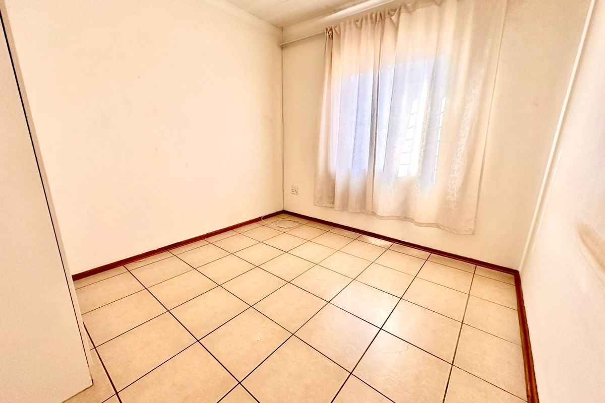 A vacant bedroom featuring neutral ceramic floor tiles, plain white walls, and a window with fitted curtain tracks.
