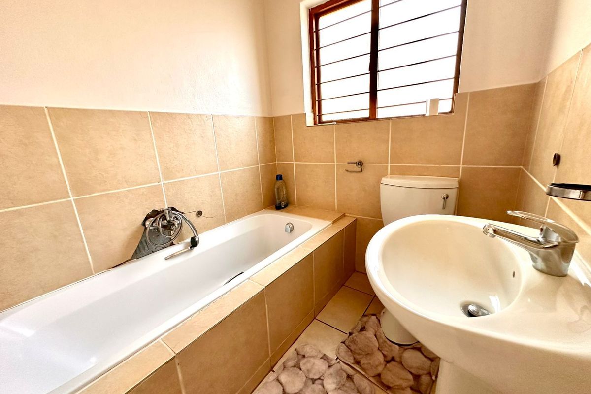 A compact bathroom featuring a tiled bathtub, pedestal basin, and toilet, with a window providing natural light.