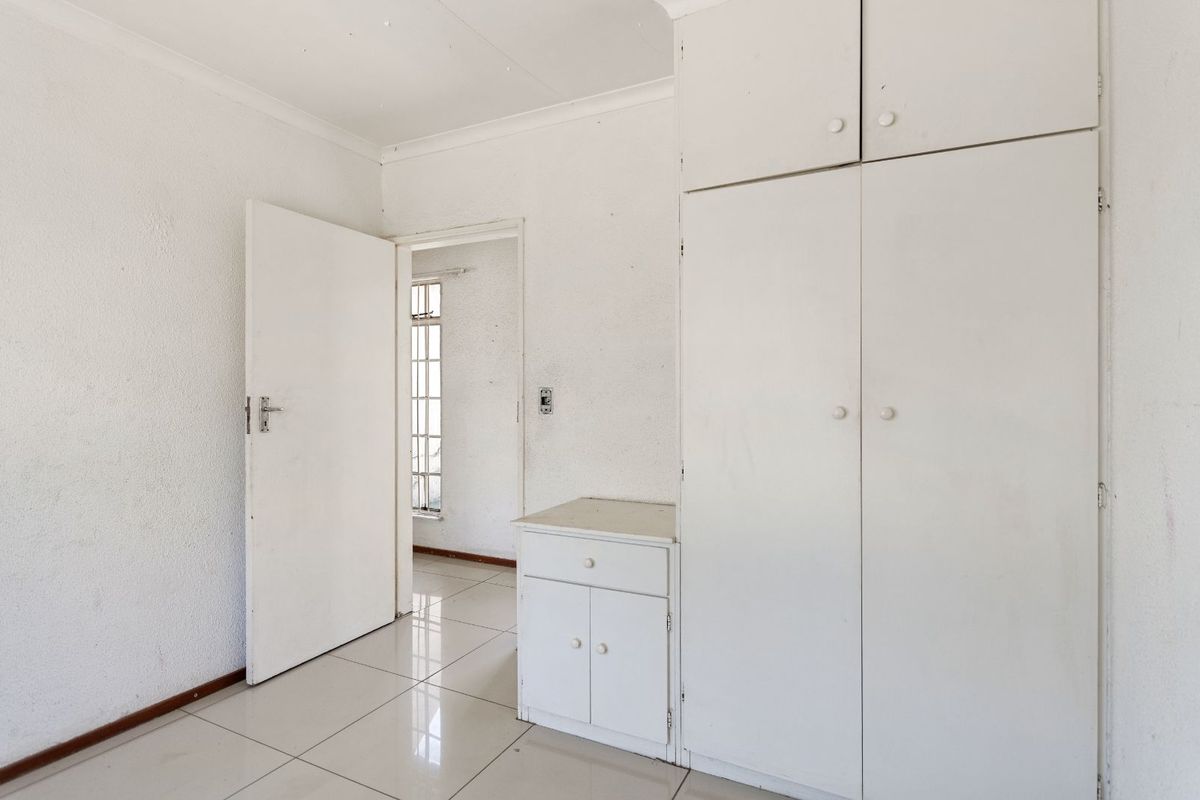 A vacant bedroom featuring built-in white cabinetry, tiled flooring, and access to an adjoining room.