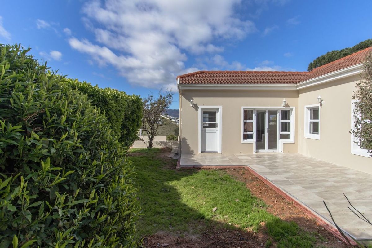 Rear view of the property featuring a tiled patio area, white framed doors and windows, and a landscaped garden with established hedges.