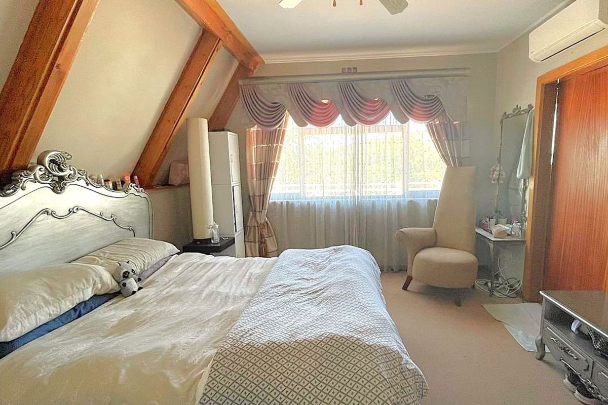 A bedroom featuring exposed timber rafters, a wall-mounted air conditioning unit, and a large window with decorative pelmet and curtains.