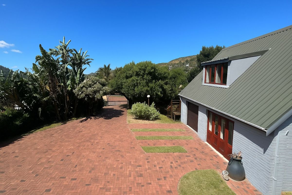 An elevated view of the property exterior featuring a paved driveway, landscaped garden area, and the side facade of the house with a garage.