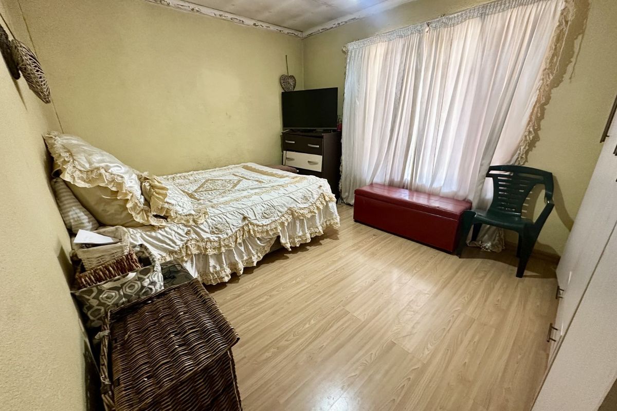 A bedroom featuring light wood-look laminate flooring and a large window with curtains, requiring cosmetic updates to the walls and ceiling.