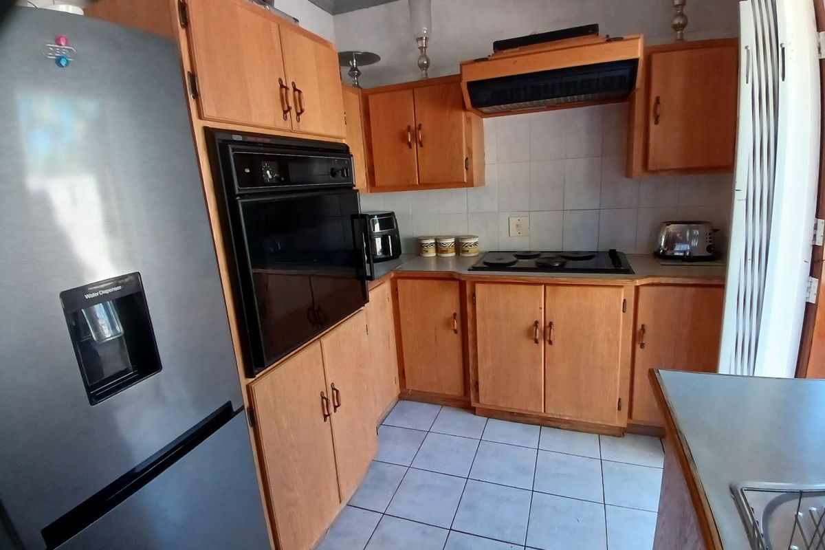 A functional kitchen featuring wooden cabinetry, a built-in oven, a hob with an extractor fan, and tiled flooring.