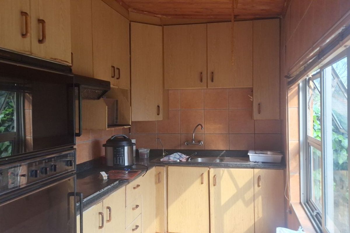 A compact kitchen featuring dated wooden cabinetry, tiled splashbacks, a built-in oven, and a sink, with large windows providing natural light.