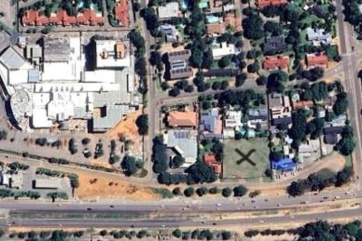 Aerial view of a vacant residential plot marked with an X, situated in a developed suburban area near commercial infrastructure.