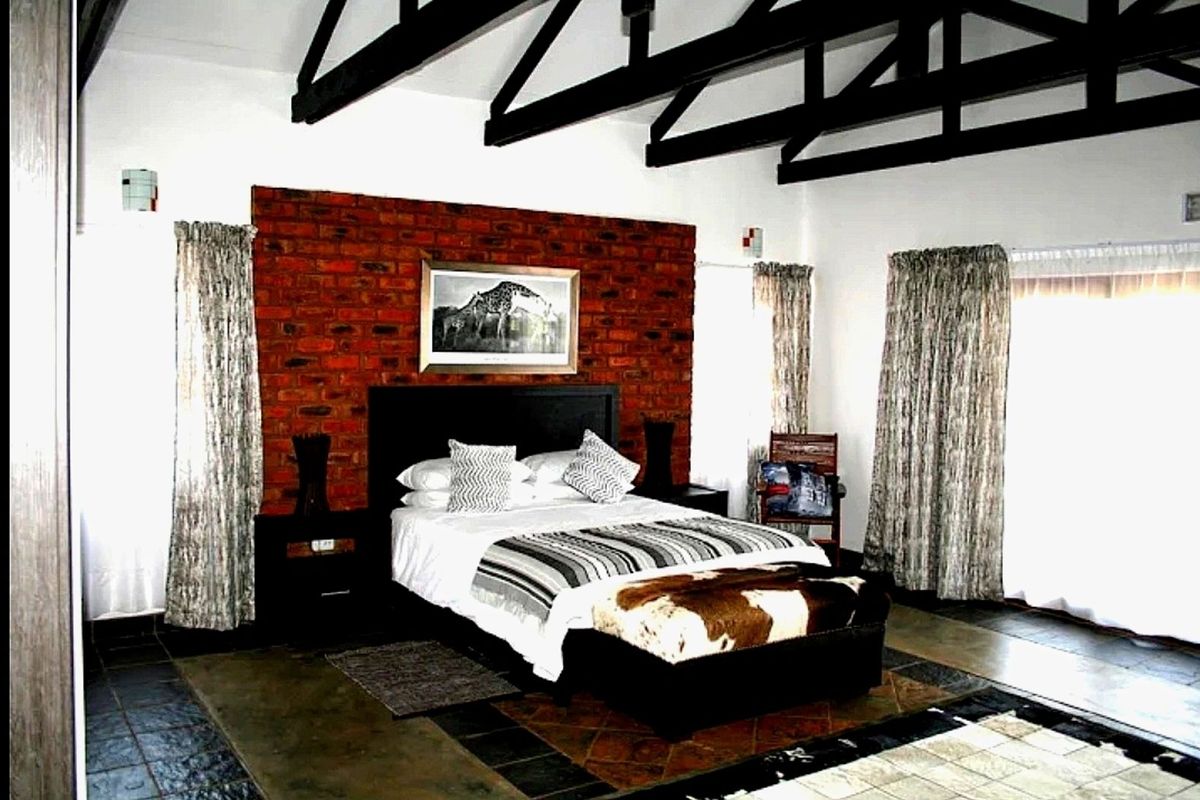 Spacious bedroom featuring exposed timber roof trusses, a rustic face-brick feature wall, and tiled flooring with direct access to the outdoors.