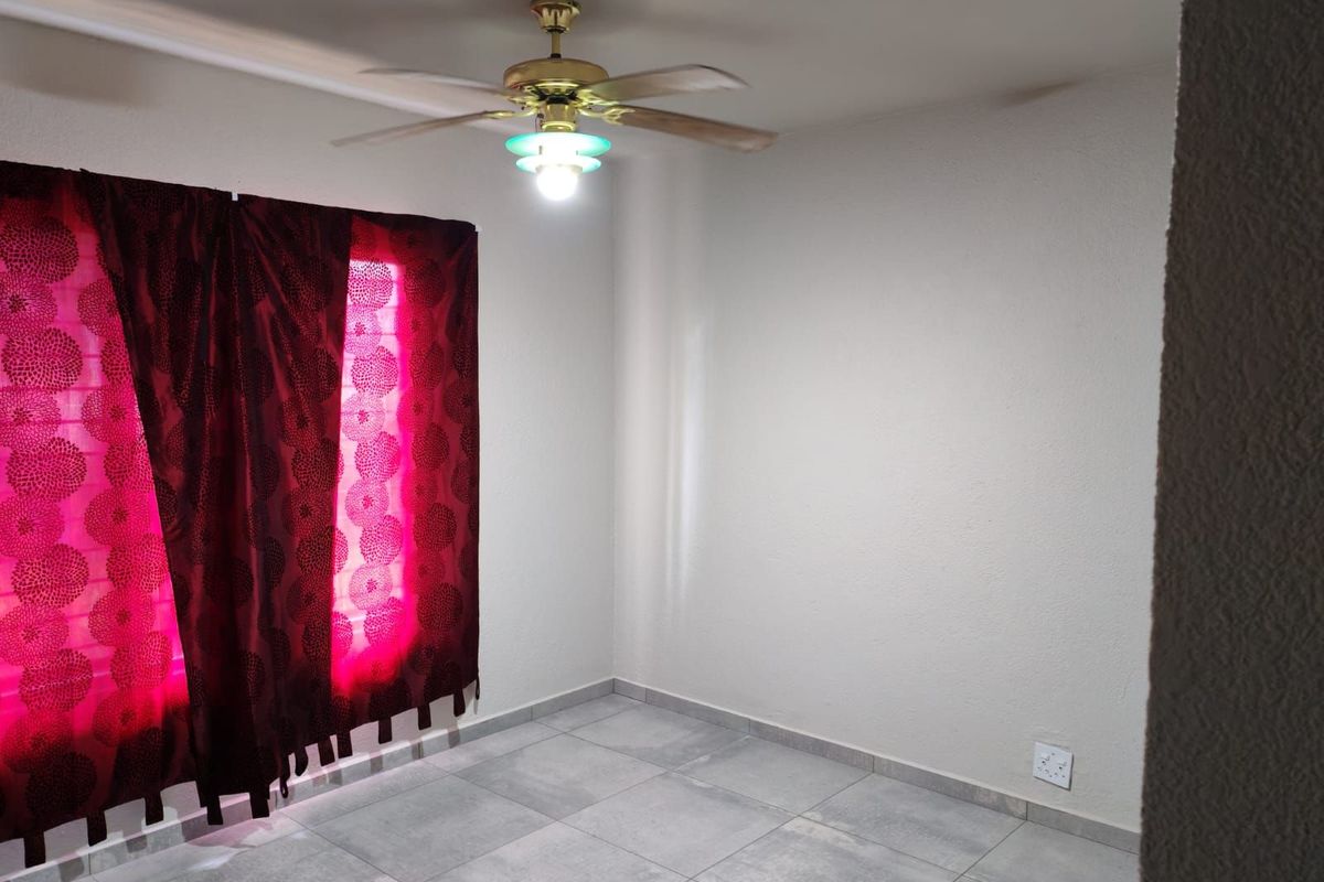 A clean, empty bedroom featuring neutral tiled flooring, a ceiling fan with integrated lighting, and large windows dressed with curtains.