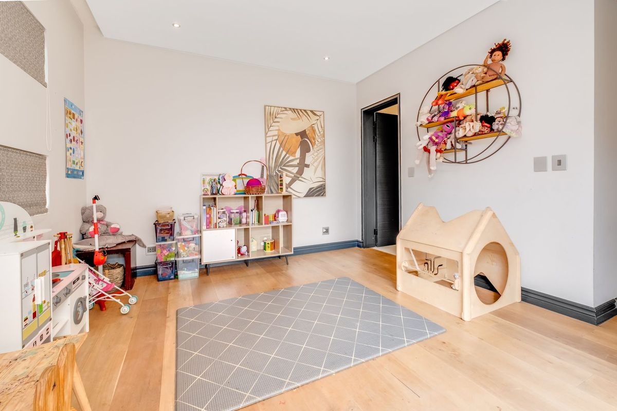A bright bedroom featuring light wood flooring, recessed ceiling lighting, and dark-framed door architraves, currently utilized as a children's play area.