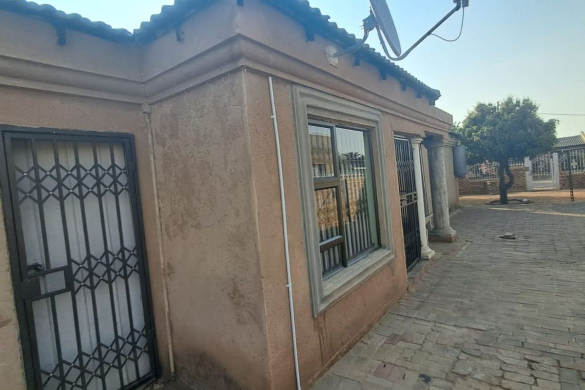 Exterior view of the property featuring a paved courtyard, security gates, and classic architectural columns along the side facade.