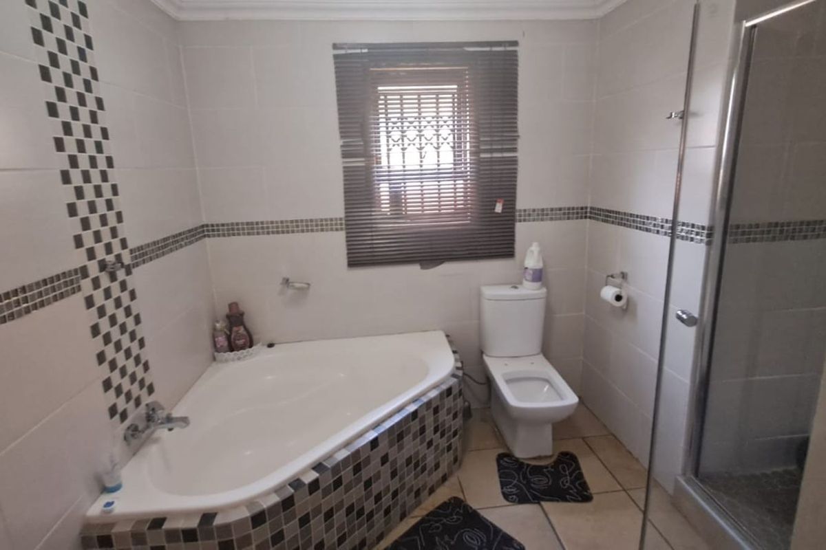 A functional bathroom featuring a corner bathtub, separate glass-enclosed shower, toilet, and tiled finishes with decorative mosaic accents.