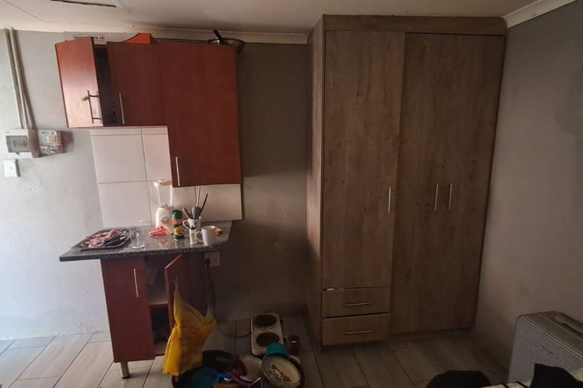 A compact kitchenette area featuring basic cabinetry, tiled splashback, and a built-in wardrobe, suitable for a studio or small living space.