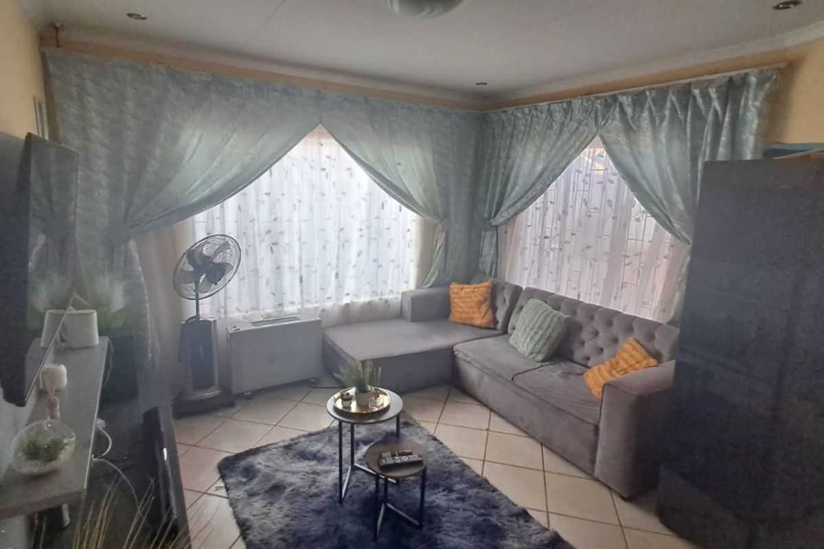 A cozy living room featuring tiled flooring, recessed ceiling lighting, and large windows with curtains, providing a comfortable and functional living space.