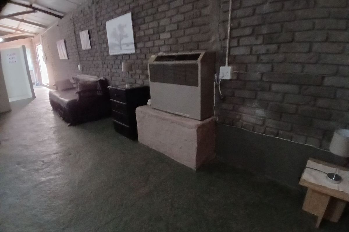 A rustic living area featuring exposed brick walls, concrete flooring, and a built-in air conditioning unit.