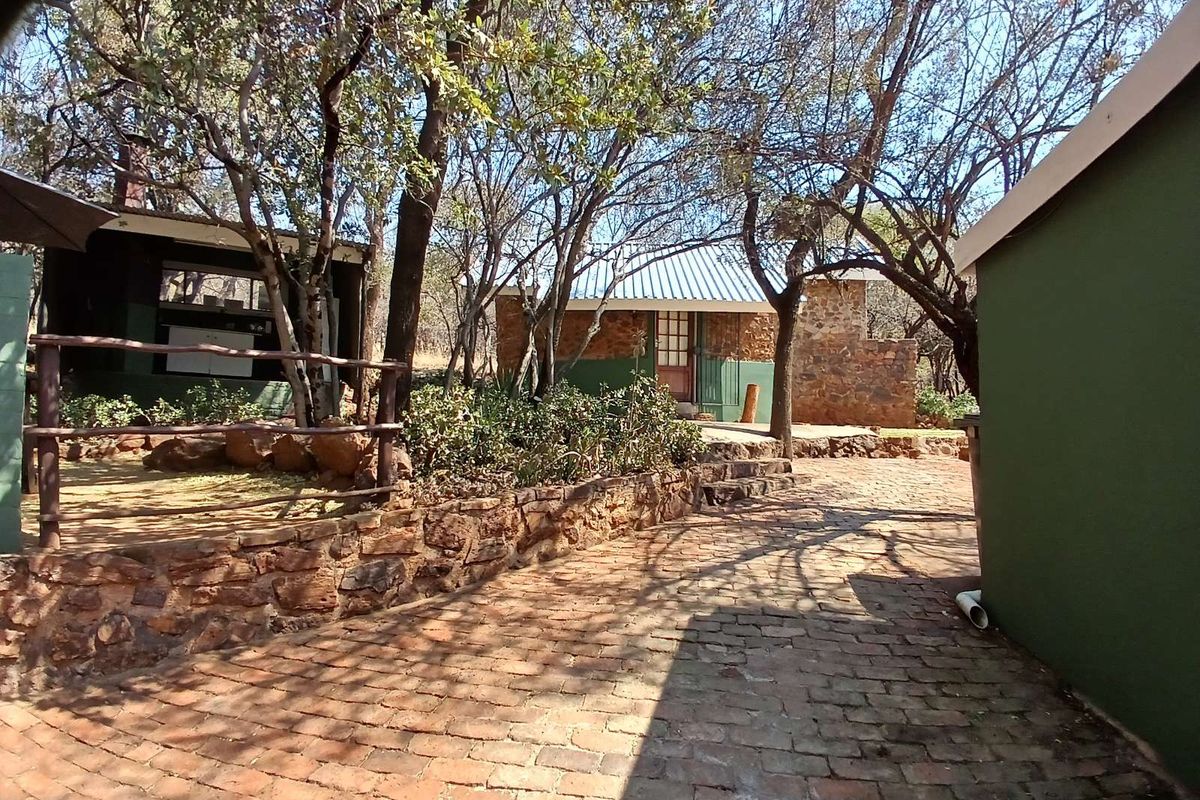 A rustic outdoor area featuring a brick-paved pathway, stone retaining walls, and mature trees surrounding the exterior of the property buildings.