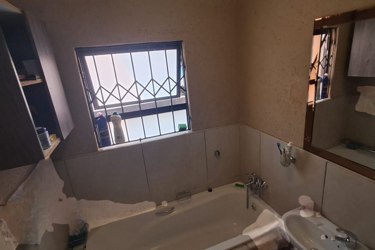 A functional bathroom featuring a standard bathtub, wall-mounted basin, and security bars on the window, requiring cosmetic updates to the wall finishes.